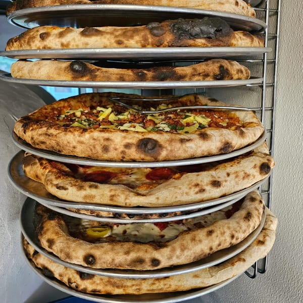 Stack of pizzas on metal trays, with one topped with chicken and peppers.