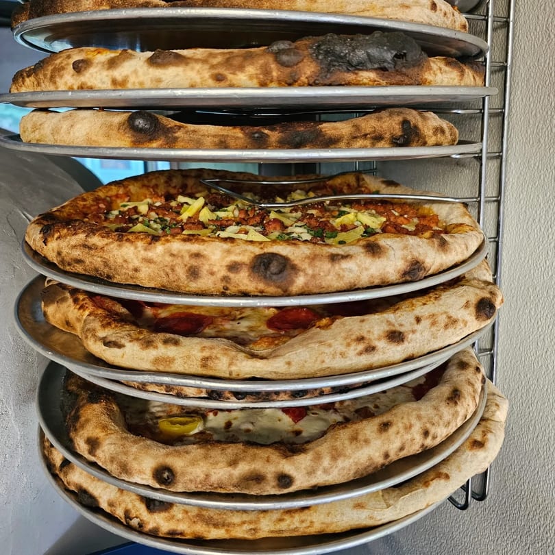 Stack of pizzas on metal trays, with one topped with chicken and peppers.