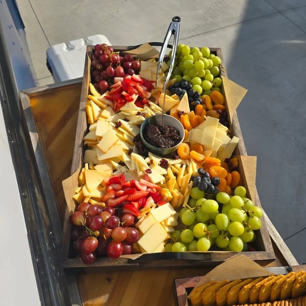 A wooden tray filled with cheese, red and green grapes, strawberries, blueberries, and dried apricots.