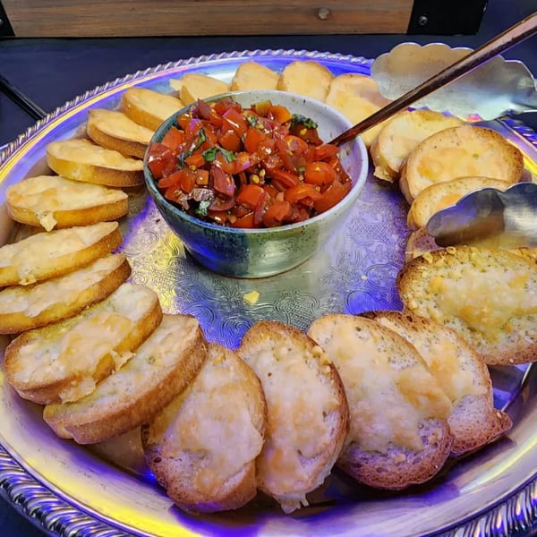 Bruschetta with diced tomatoes and basil in a bowl, surrounded by toasted bread slices on a silver tray.
