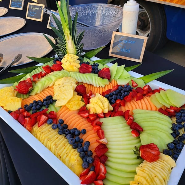 A large white platter filled with sliced cantaloupe, honeydew, pineapple, strawberries, and blueberries.