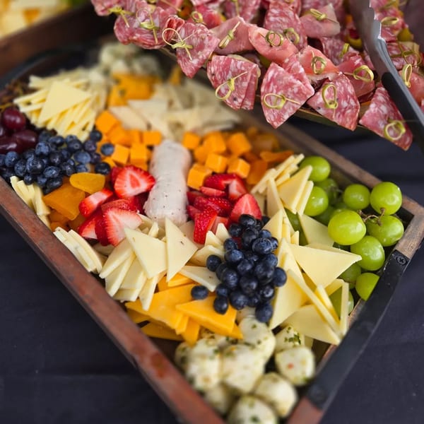 A wooden tray filled with cheeses, blueberries, strawberries, grapes, and sliced meats.