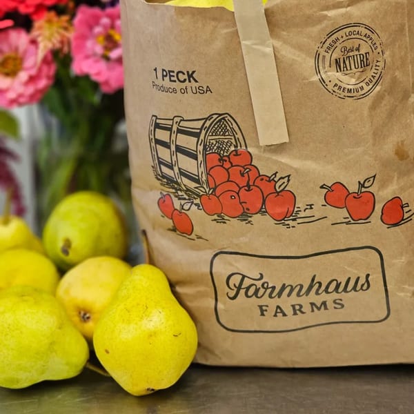 A brown paper bag from Farmhaus Farms with an apple illustration, surrounded by fresh yellow pears.