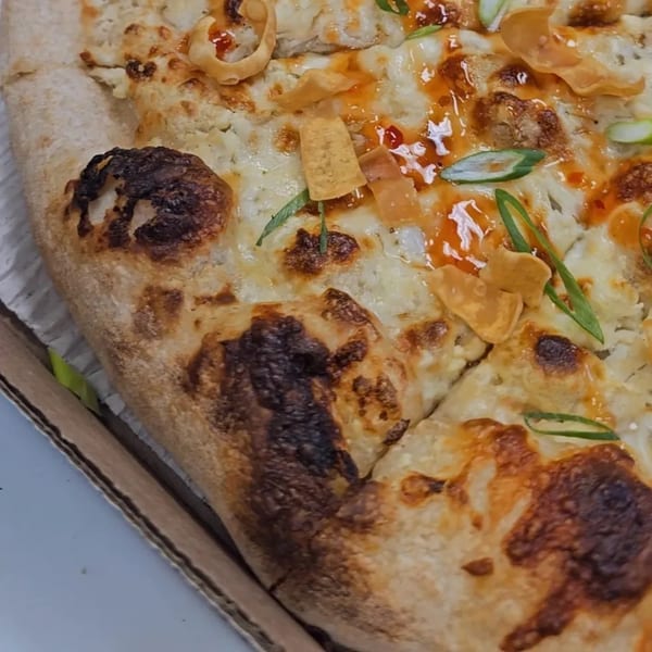 Close-up of a pizza with white sauce, cheese, green onions, and crispy toppings in a box.