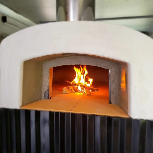 A white wood-fired pizza oven with a roaring fire inside, ready for cooking.