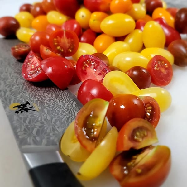 A chef's knife rests beside a colorful assortment of whole and halved cherry tomatoes.