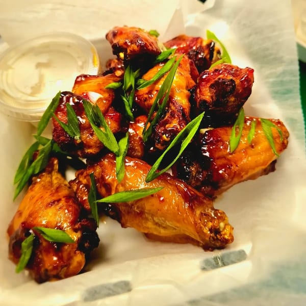 Sweet and spicy chicken wings garnished with green onions, served with a side of ranch.