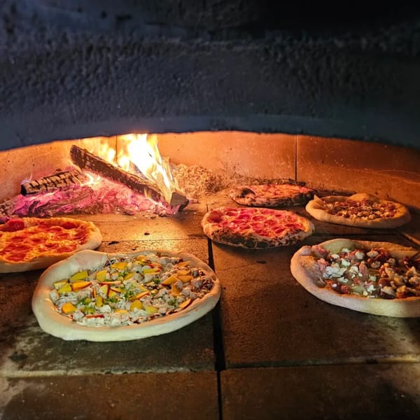 Multiple pizzas baking inside a wood-fired oven with glowing embers and flames.