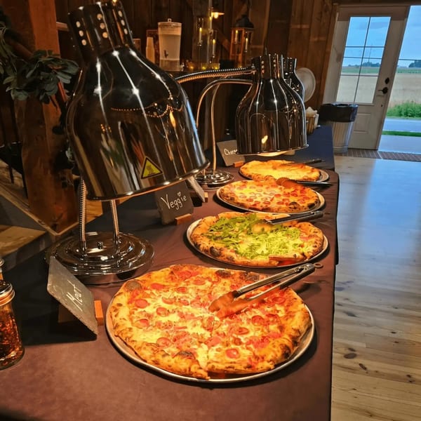 A buffet table with several pizzas under heat lamps, including veggie and meat options.
