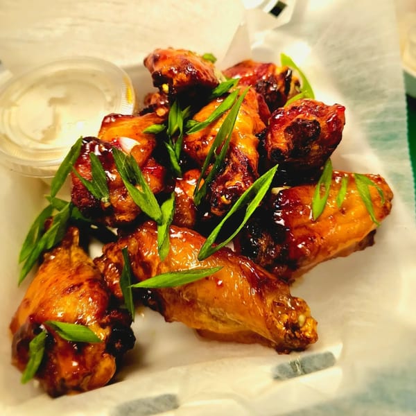 Glazed chicken wings topped with fresh green onions, served with a side of ranch dressing.
