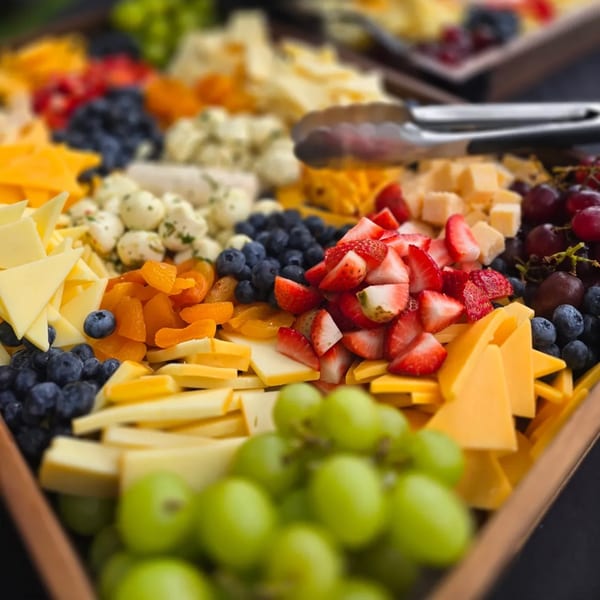 A vibrant charcuterie board filled with various cheeses, strawberries, blueberries, grapes, and dried apricots.