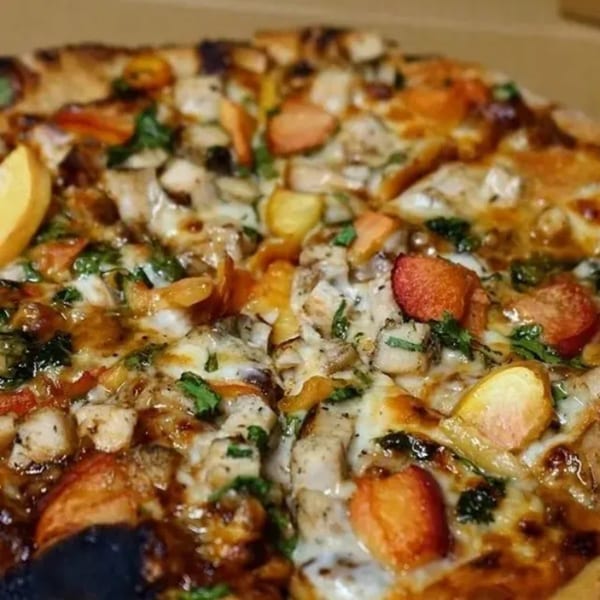 Close-up of a pizza with chicken, bell peppers, and melted cheese, glistening with sauce.