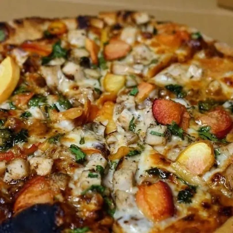 Close-up of a pizza with chicken, bell peppers, and melted cheese, glistening with sauce.