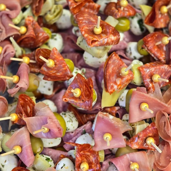 Close-up of numerous charcuterie skewers with salami, ham, olives, mozzarella, and artichoke hearts.