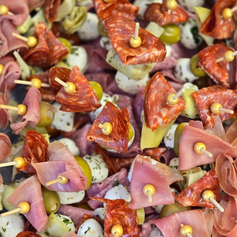 Close-up of numerous charcuterie skewers with salami, ham, olives, mozzarella, and artichoke hearts.