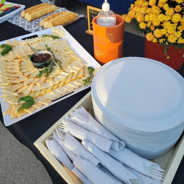 A buffet table with cheese and crackers, hand sanitizer, and yellow potted flowers.