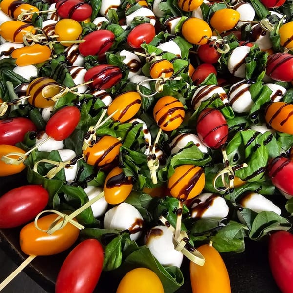 Caprese skewers with red and yellow tomatoes, mozzarella, basil, and balsamic glaze.
