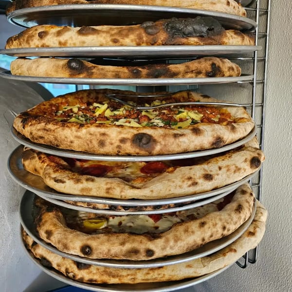 Multiple pizzas with crispy crusts and various toppings stacked on metal racks, ready to be served.