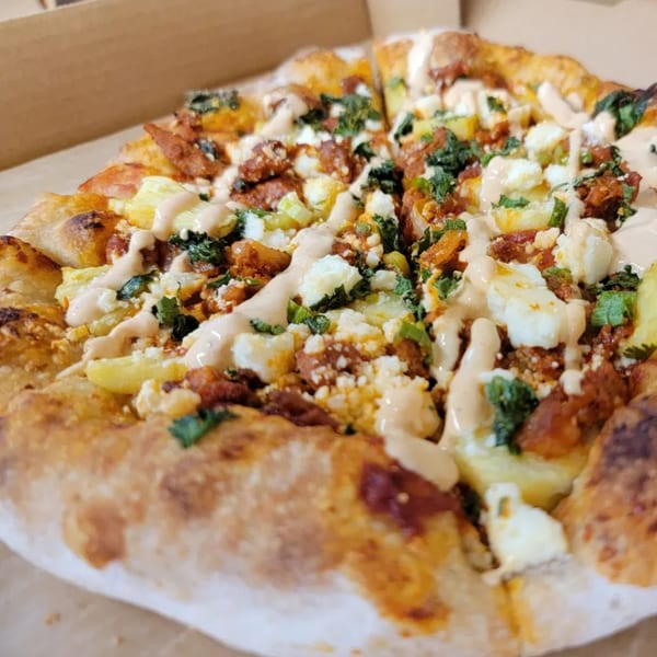 Close-up of a pizza with chorizo, potatoes, cheese, cilantro, and a creamy sauce in a box.